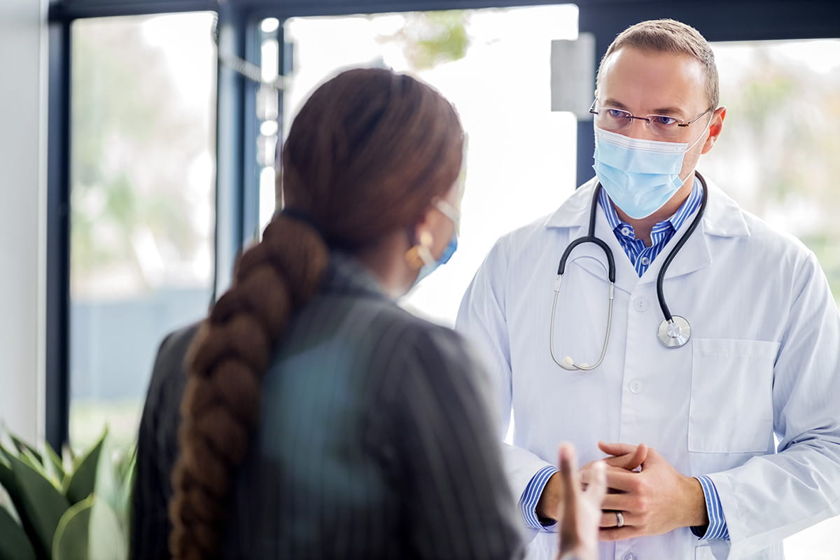 Masked doctor discusses treatment options with family member.