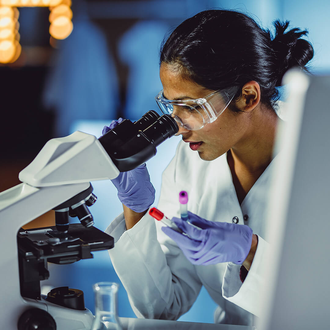 An oncology and hematology specialist examining medical samples under a microscope.