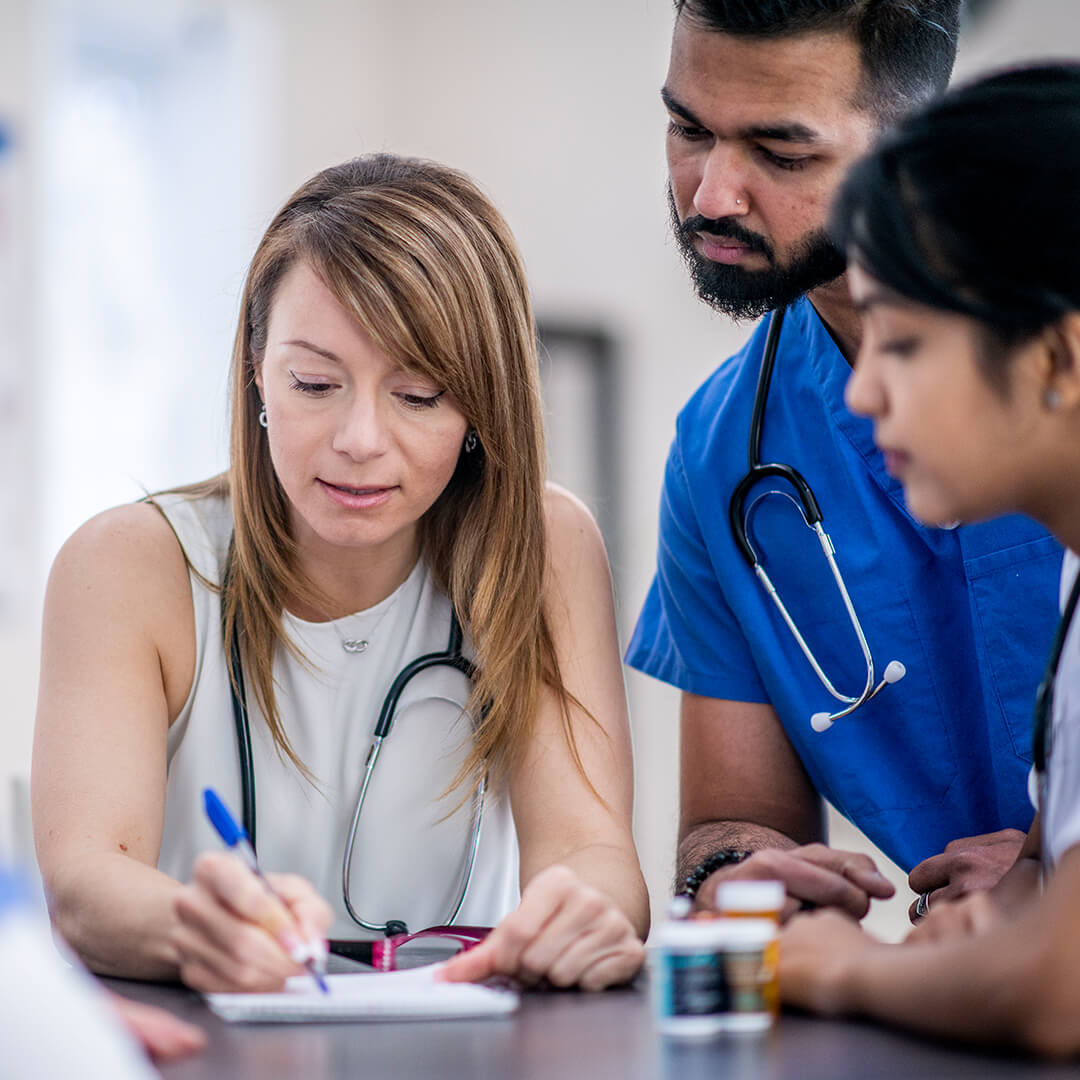 A woman drawing on a notepad while a doctor and another person look over their shoulder