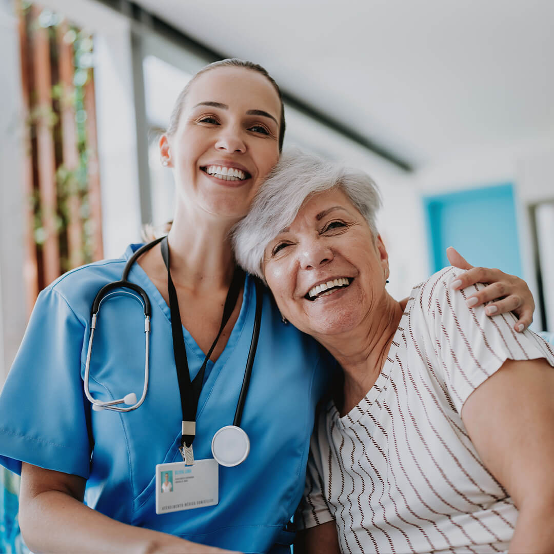 An elderly woman hugging a female doctor around the shoulder, both smiling for a photo