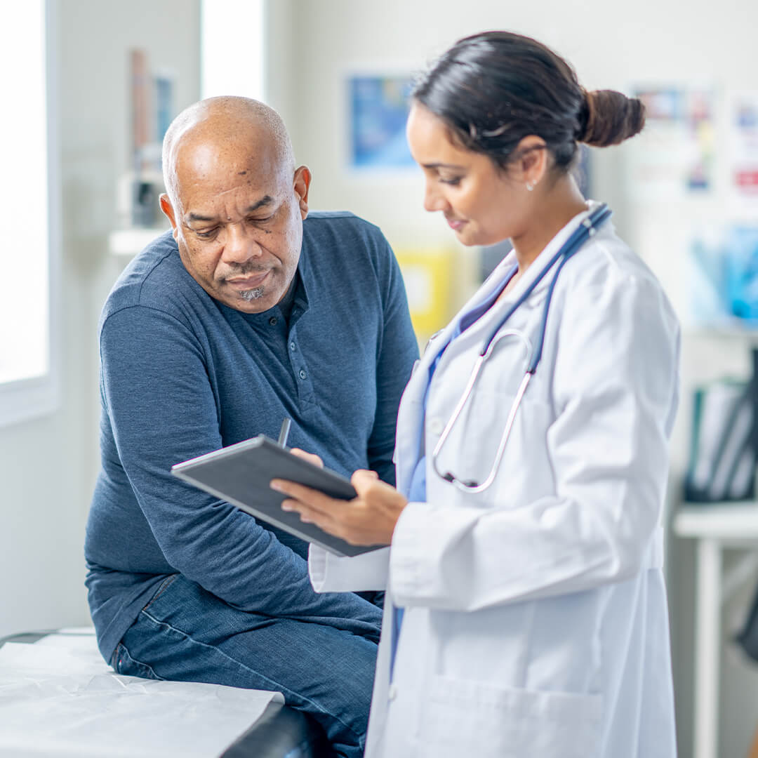 An oncologist shows a patient his medical records on a tablet in a clean hospital setting.